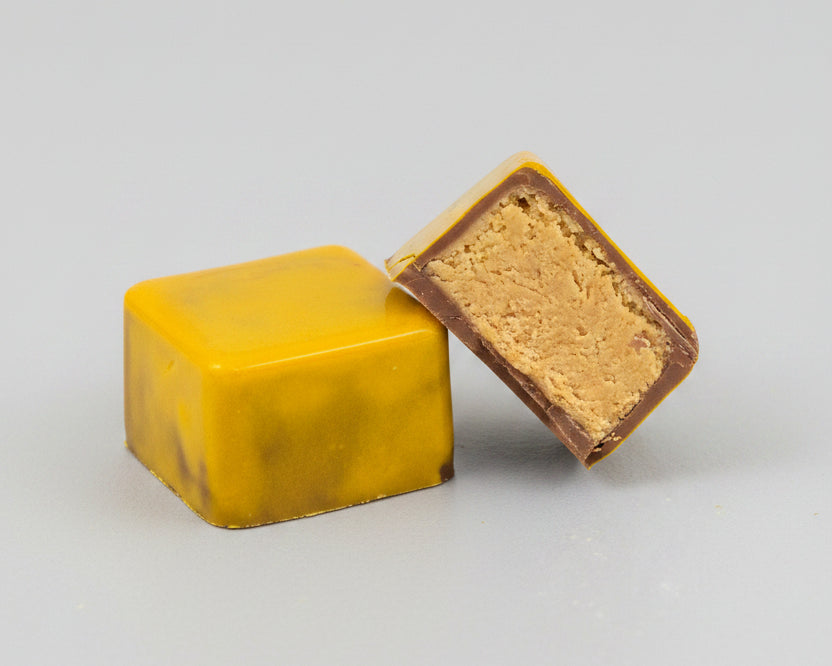Two milk chocolate peanut butter bonbons hand painted in yellow cocoa butter,  with one chocolate broken in half to show the peanut butter filling